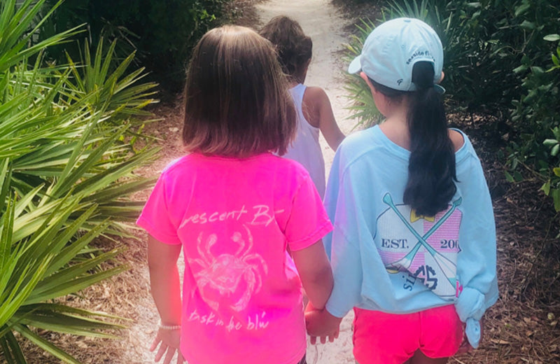 Two little girls hold hands and walk down a sidewalk.