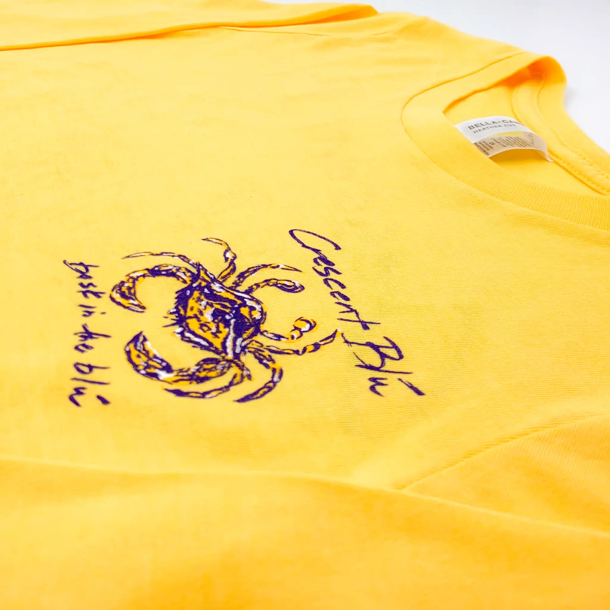 close up of Crescent Blu purple and gold crab collection logo on front left chest
