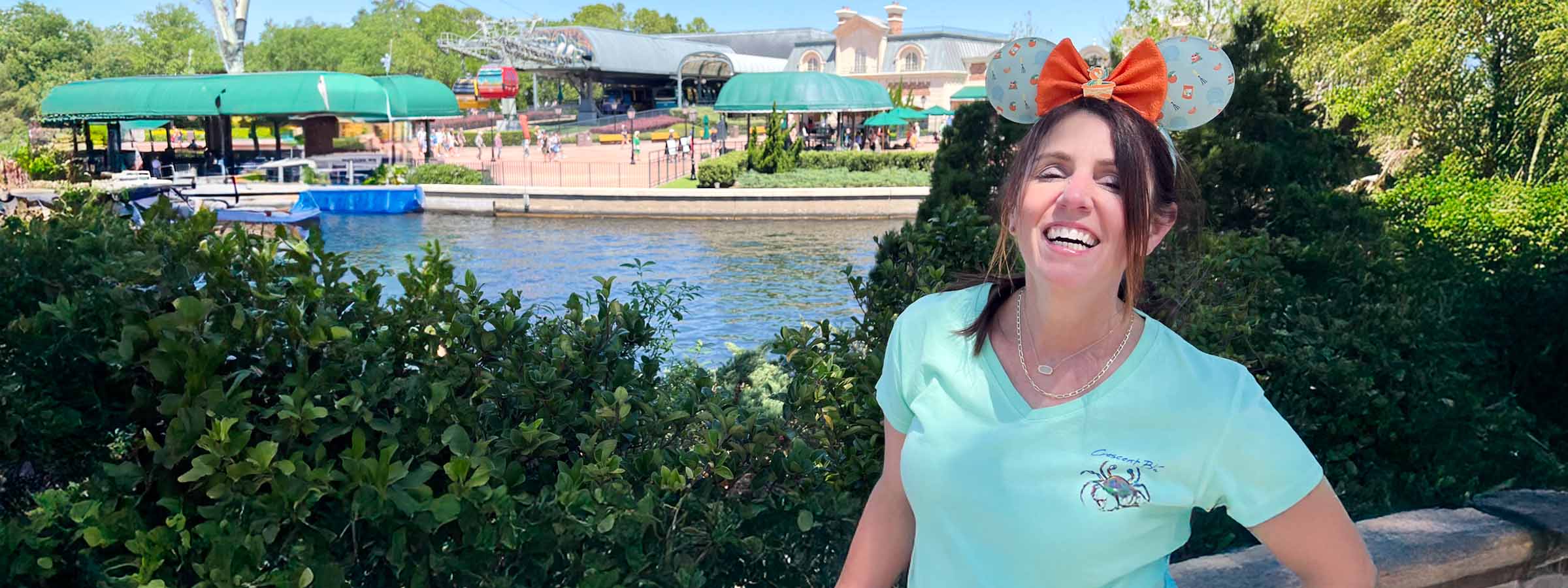 A woman wearing a Crescent Blú women's shirt, and Minnie Mouse Ears, laughs near a river in Disney World's EPCOT.