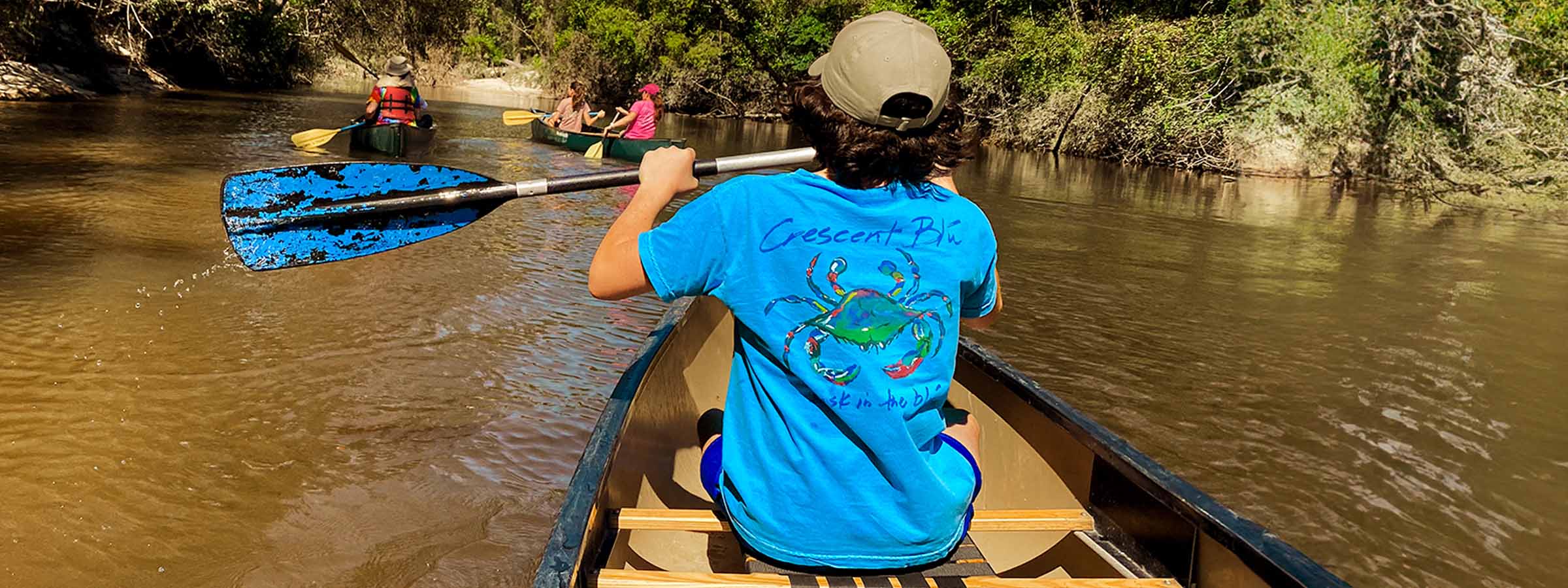 A child wearing a Crescent Blú youth t-shirt is paddling a canoe.."