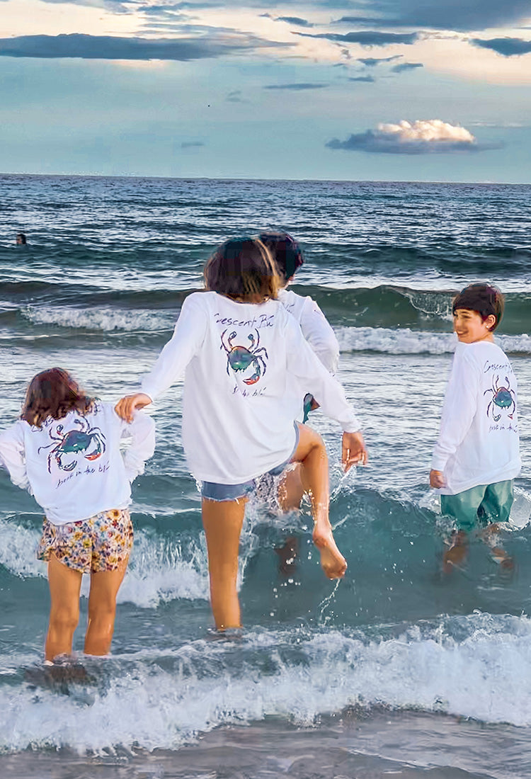 Kids in matching white tee shirts play in the ocean waves.