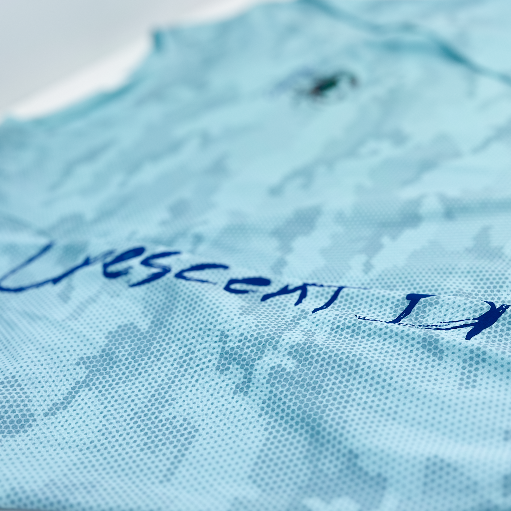 Close up of right sleeve with Crescent Blu printed along its length on aqua camo Sun shirt