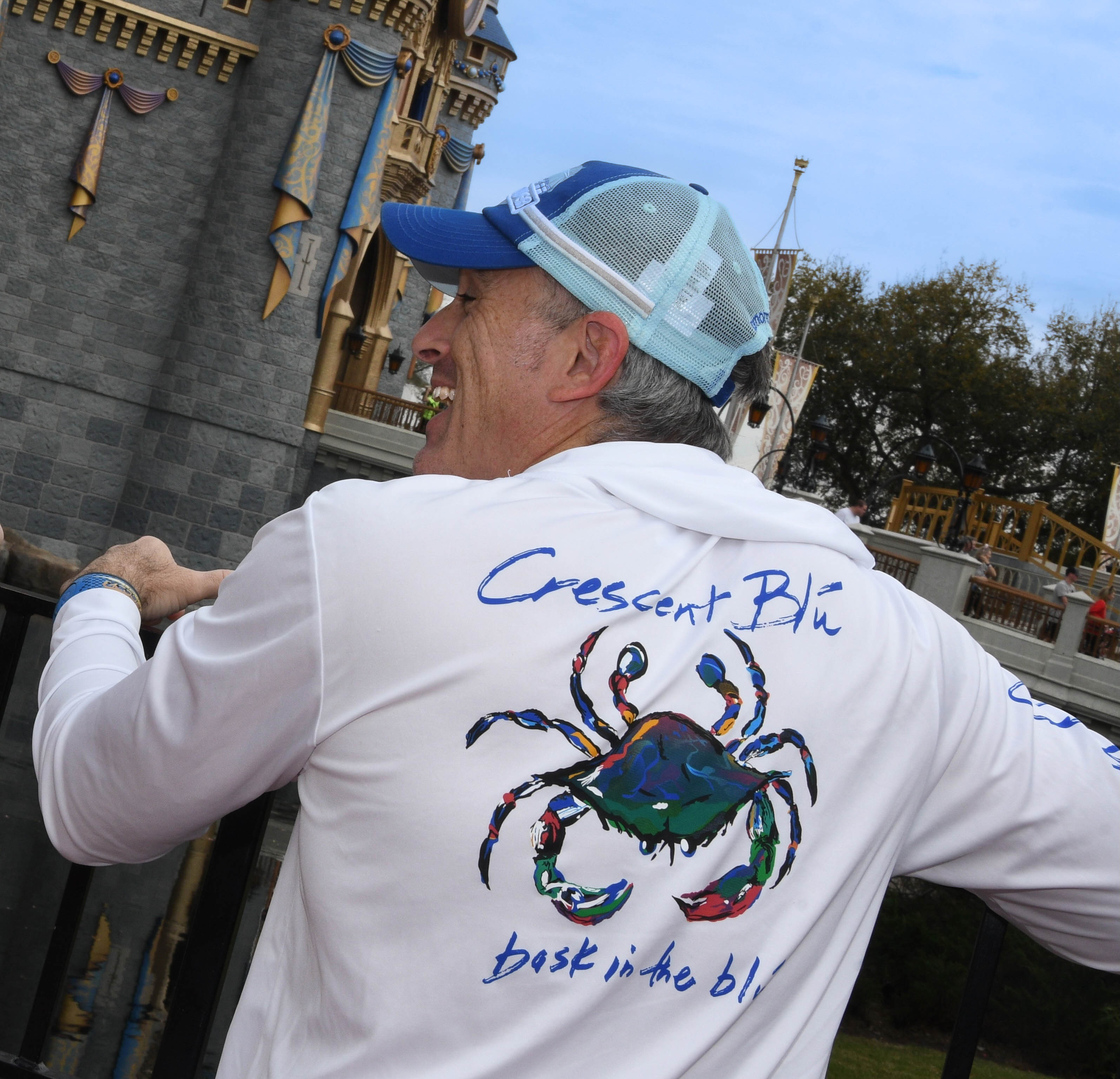 Man in a blue and white hat land a white shirt with a crab on the back is laughing. 
