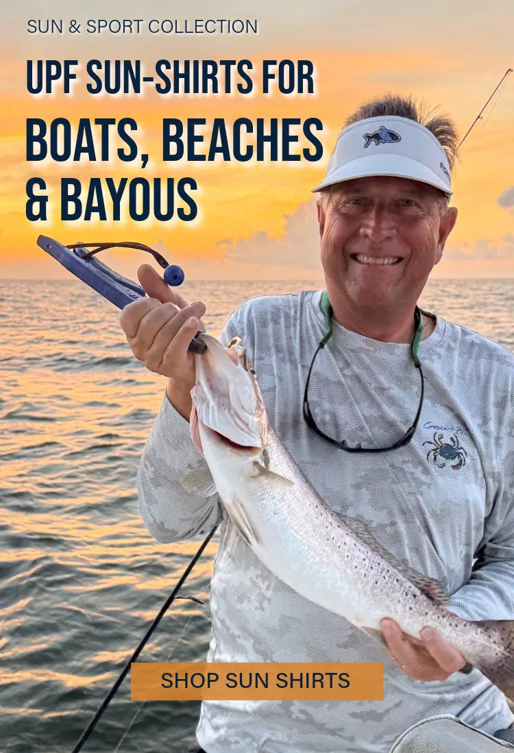 A man wearing a Crescent Blú Signature Crab UPF sun shirt while holding a fish on a boat at sunset.