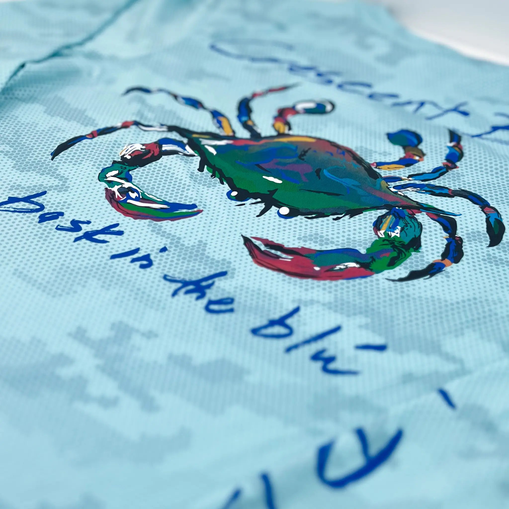 Close up of vivid multi-colored Crescent Blu Signature crab logo on back of Aqua Camo Performance Sun Shirt