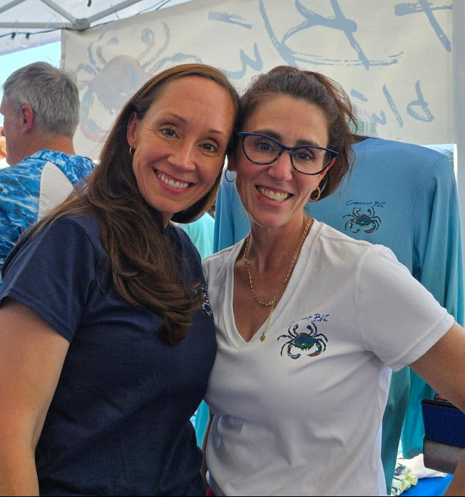 Two women posing together under a tent with a blue shirt featuring a crab design.